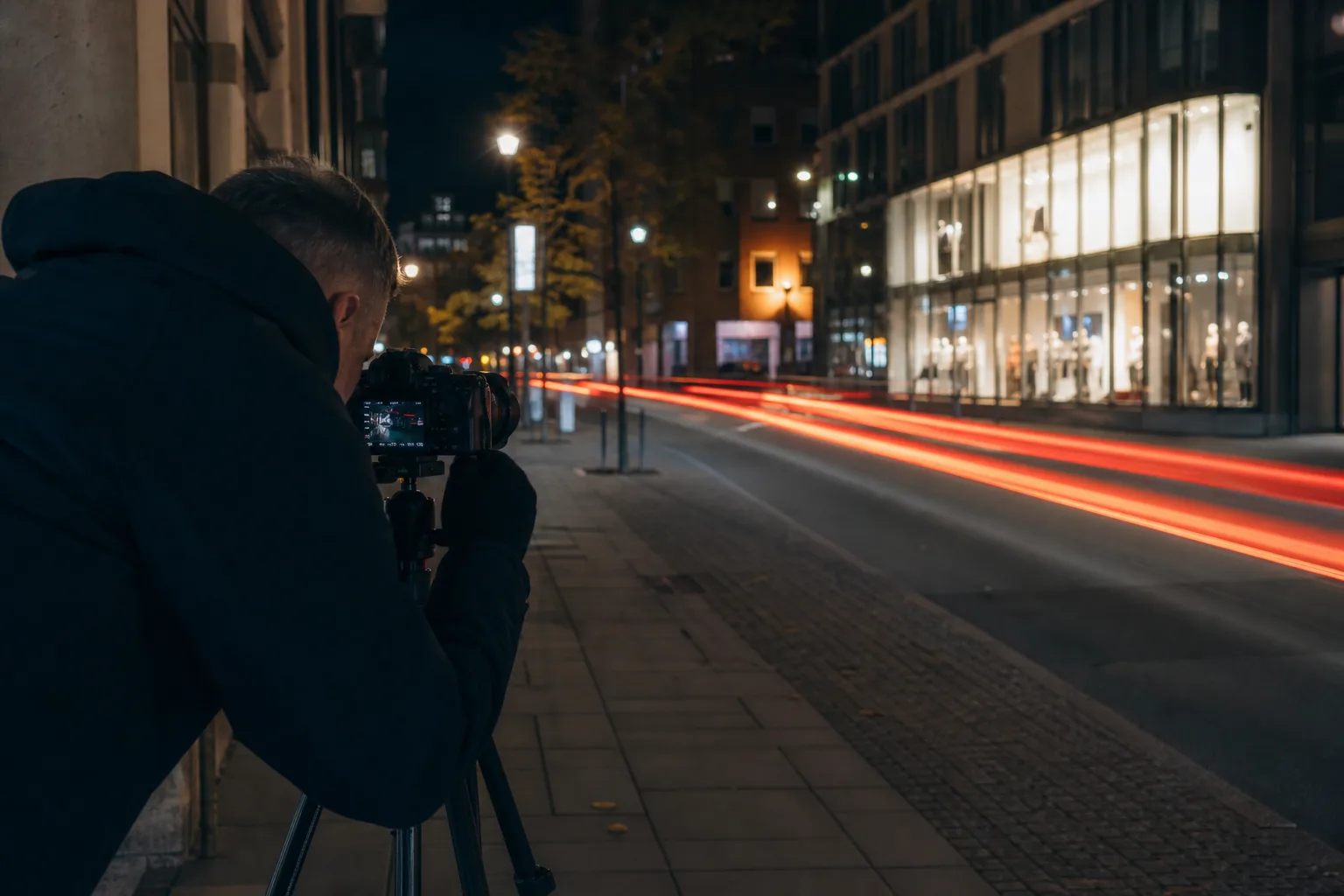 Nattfotografering av en stadsgata med ljusspår från bilar och upplysta skyltfönster