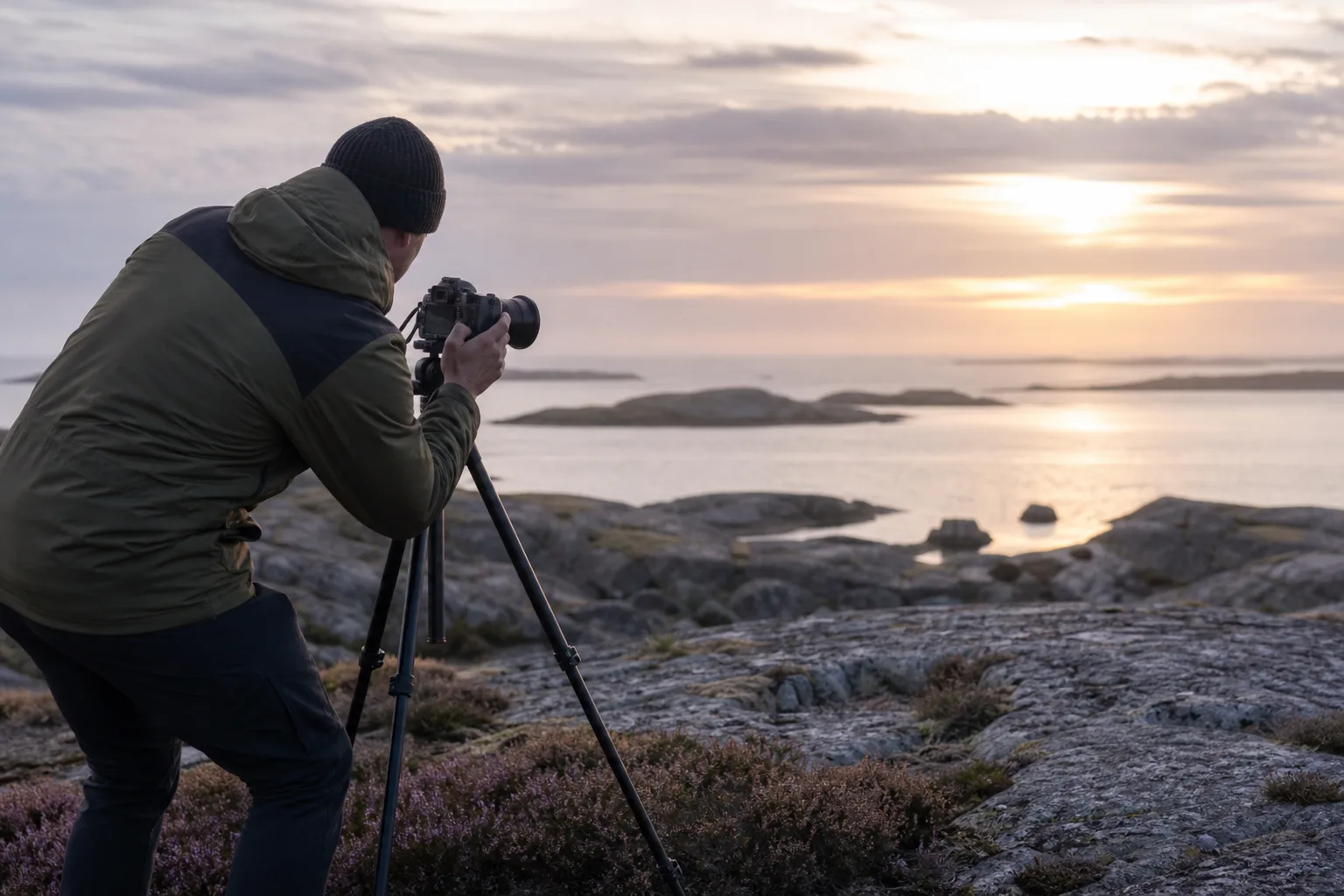 Fotograf med stativ och vidvinkelobjektiv vid en klippa i naturen